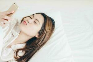porträtt av asiatisk kvinna spelar mobil telefon på de säng. foto