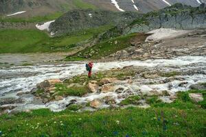 professionell fotograf skjuter en landskap stående på en små grön ö i de mitten av en stormig berg flod. grön alpina highlands foto