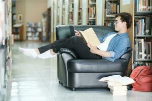 studerande Sammanträde på soffa och studerar på bibliotek. foto