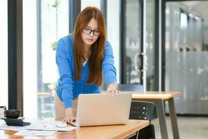 ung asiatisk affärskvinna arbetssätt på kontor använder sig av bärbar dator. foto
