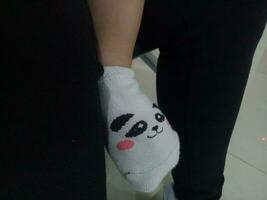 Foto av en bebis fot i en strumpa med en söt panda ansikte på den