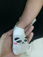 Foto av en bebis fot i en strumpa med en söt panda ansikte på den