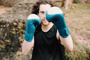 en ung man med långt hår som gör boxning och kampsport i parken med boxhandskar och seriöst ansikte