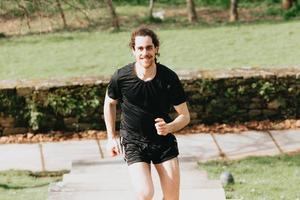 en ung och atletisk man som springer på övervåningen medan du tränar kondition i en park under en solig dag foto