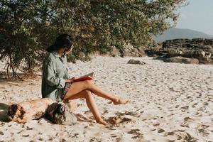 ung marockansk kvinna på moderna kläder sitter på stranden läser en bok under en solig dag med kopia utrymme inspirerande och koppla av tema med färgglada toner foto