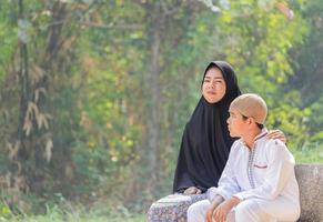 muslimska mor och son sitter på morgonen på en trädgårdsbänk