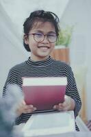 asiatisk flicka innehav stor skola bok i hand och toothy leende med lycka foto