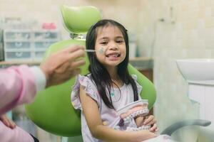 asiatisk tandläkare och asiatisk pojke kunskap handla om tandställning använda sig av tandprotes modell när mor sitta förbi i dental klinik foto