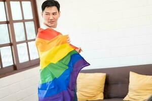 glad ung asiatisk Gay man insvept i regnbåge flagga njuter i Hem. homosexuell lgbtiq begrepp, regnbåge flagga, fira parad. kopia Plats. foto