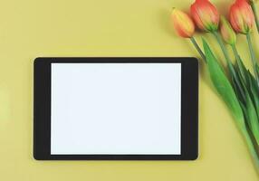 platt lägga av digital läsplatta med tom vit skärm, tuip blommor isolerat på gul bakgrund. foto