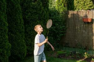 en Lycklig pojke innehar en badminton racket i hans händer, spelar sporter utanför i sommar foto