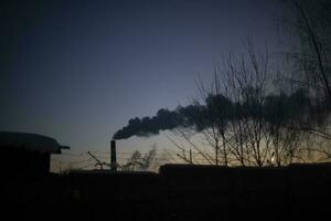 rök från skorsten på solnedgång. kväll landskap med fabrik. rök i himmel. foto