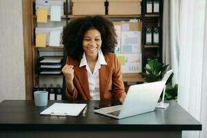 afrikansk företag kvinna är förtjust och Lycklig med de arbete de do på deras läsplatta, bärbar dator och tar anteckningar på de kontor. foto