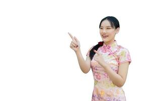 ung asiatisk kvinna vem bär rosa Cheongsam klänning i kinesisk ny år tema medan henne hand punkt visar till närvarande något och utseende på kamera leende lyckligt med isolerat på vit bakgrund. foto