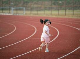 bebis asiatisk flicka springa joggning på löpning Spår, löpning fält på stadion. liten flicka löpning på solnedgång Lycklig bebis flicka leende. liten flicka löpning på solnedgång. söt bebis flicka löpning på löpning Spår. foto