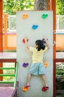 söt asiatisk flicka leende klättrande stege och spela på skola eller dagis gård eller lekplats. friska sommar aktivitet för barn. liten asiatisk flicka rolig Lycklig. barn spelar på utomhus- lekplats. foto