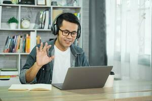 asiatisk frilans företag man bär hörlurar framställning video ring upp i Hem kontor, använder sig av bärbar dator, talande, tittar på webinar eller studerar språk, tala, uppkopplad Träning, förklara, e-lärande. foto