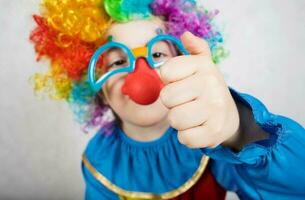 pojke av fem år klädd i de kostym av en clown och rolig glasögon med röd näsa visar hans näve foto