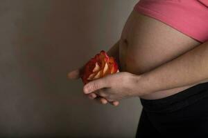 ung gravid kvinna håller naturlig reste sig blomma stänga till henne mage. foto