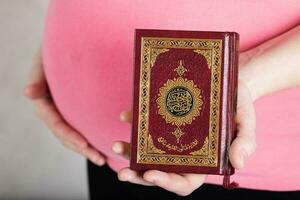 ung gravid kvinna håller järnek bok av koranen. foto