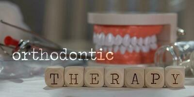 ord ortodontisk terapi sammansatt av trä- tärningar. biljard, dokument, penna, mänsklig käke modell i de bakgrund. foto