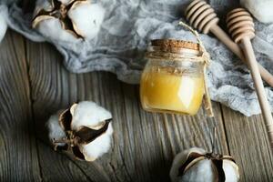 bomull honung i en glas flaska på en trä- yta. foto