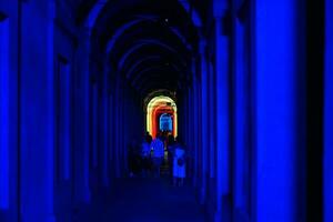 Bologna, Italien- juni 23, 2023-människor promenad på natt under de arkader ledande till de fristad av san luca upplyst för de först utgåva av de bologna arkader festival. foto