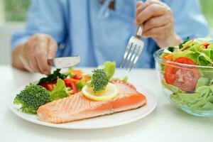 asiatisk äldre kvinna patient äter lax insats och vegetabiliska sallad för friska mat i sjukhus. foto