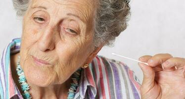 gammal kvinna är rengöring henne öron med bomull svabb foto