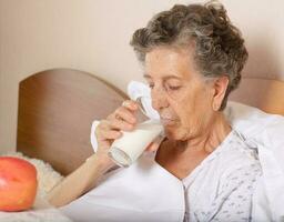 gammal kvinna drycker några mjölk i de morgon- foto