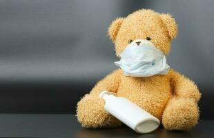en plysch teddy Björn i en medicinsk mask med en flytande tvål dispenser. foto