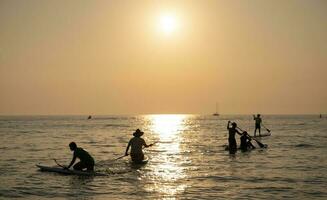 juni 21, 2021. pattaya thailand. grupp av människor på stå upp paddla styrelse på tyst hav på solnedgång eller soluppgång. och ljus solnedgång foto