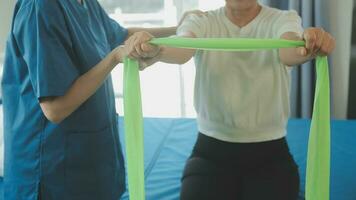 Lycklig senior kvinna håller på med övning på Hem med fysioterapeut. gammal pensionerad lady håller på med stretching vapen på Hem med de hjälp av en personlig tränare under en rehabilitering session. foto