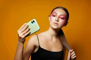 ung skön kvinna utseende på de telefon ljus smink Framställ mode känslor gul bakgrund oförändrad foto