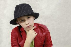 porträtt av en fundersam pojke i ett elegant hatt och röd jacka. modern barn. foto
