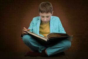 en pojke i en kostym sitter med en bok på en brun bakgrund. foto