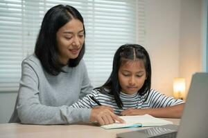 mor undervisning lektion för dotter förbi bärbar dator. asiatisk ung liten flicka lära sig på Hem. do läxa med snäll mor hjälp, uppmuntra för examen. Asien flicka Lycklig hemskola. mamma ge råd utbildning tillsammans. foto