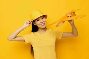 charmig ung asiatisk kvinna glad kvinna med ett flygplan i de händer av roligt gul bakgrund oförändrad foto