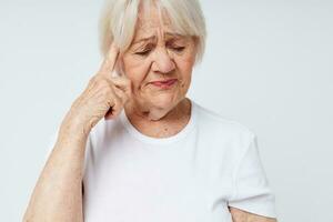 emotionell äldre kvinna i en vit t-shirt huvudvärk hälsa problem ljus bakgrund foto