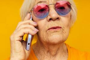 äldre kvinna talande på de telefon i gul glasögon gul bakgrund foto