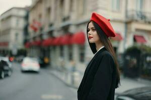 mode kvinna porträtt skönhet stående på de gata i främre av de stad i eleganta kläder med röd mun och röd basker, resa, filmiska Färg, retro årgång stil, urban mode livsstil. foto