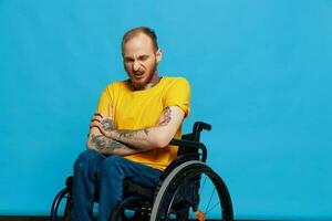 en man i en rullstol i en t-shirt med tatueringar på hans vapen sitter på en blå studio bakgrund, en full liv, en verklig person foto