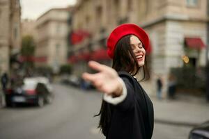 mode kvinna leende med tänder stående på de gata i främre av de stad turist Följ mig eleganta kläder med röd mun och röd basker, resa, filmiska Färg, retro årgång stil, urban mode. foto
