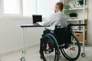 en man rullstol affärsman med tatueringar i de kontor Arbetar på en bärbar dator uppkopplad, företag bearbeta, en rullstol närbild, integration in i samhälle, de begrepp av arbetssätt en person med funktionshinder foto