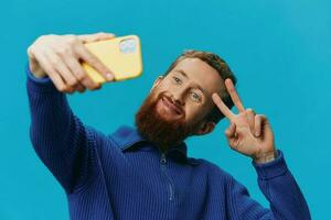 porträtt av en man med en telefon i hans händer bloggare tar selfies, på en blå bakgrund. kommunicerar uppkopplad social media, livsstil foto