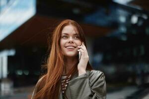 kvinna gående runt om stad och talande på de telefon i trendig kläder mot en bakgrund av lång stad byggnader med en leende foto