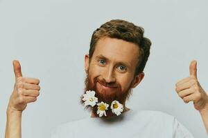 porträtt av en rolig man i en vit t-shirt med blommor daisy i hans skägg på en vit isolerat bakgrund, kopia plats. Semester begrepp och grattis. foto