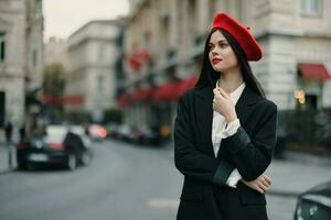 mode kvinna porträtt stående på de gata i främre av de stad i eleganta kläder med röd mun och röd basker, resa, filmiska Färg, retro årgång stil, urban mode livsstil. foto