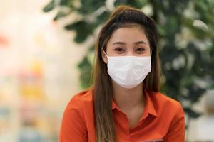 ung kvinna som bär ansiktsmask skyddande sammanträde i kafé foto