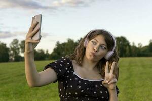 en Tonårs flicka i en klänning lyssnar till musik på en smartphone foto